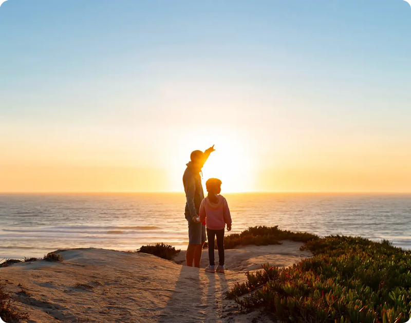 Adult and child looking out at the ocean during sunset